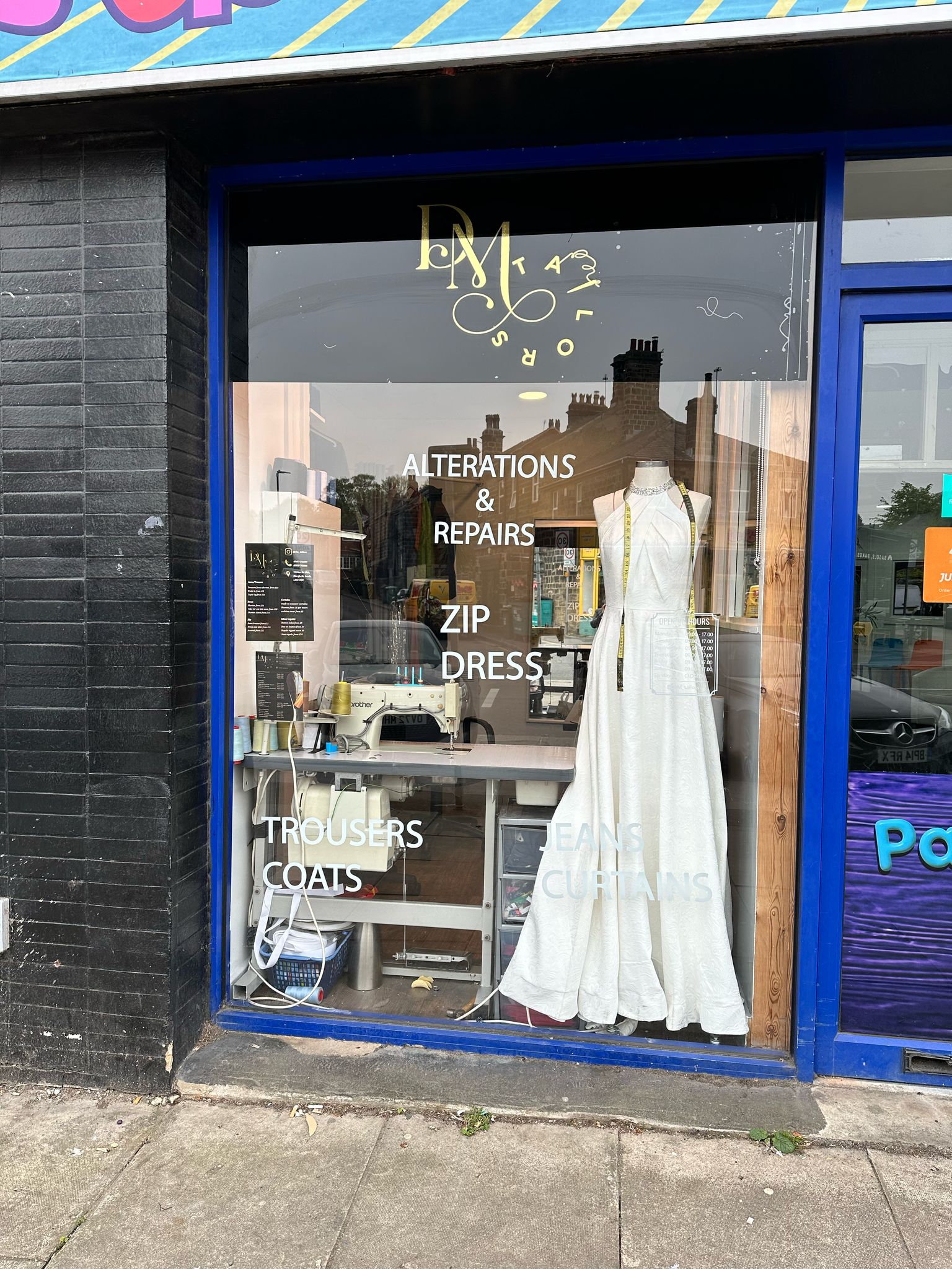 The DM Tailors shop window on New Road Side, with its gold logo and alterations sign